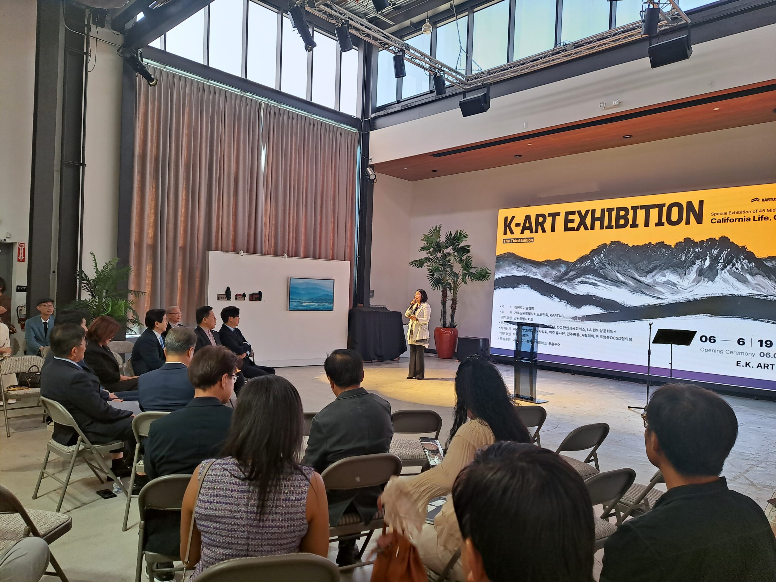 Opening reception of the K-ART Exhibition at E.K. Art Gallery in Los Angeles, California (2026). Guests attend the official opening event in front of the exhibition stage and presentation screen.
